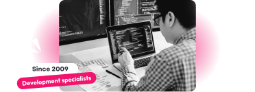 A black-and-white image of a developer working at a desk with a laptop displaying code